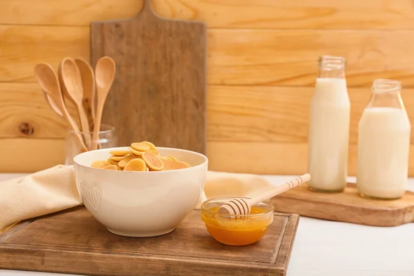 Bowl with tasty pancakes, honey and bottles of milk on wooden background