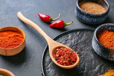 Koyu arkaplanda farklı baharatlar bulunan kâseler ve kaşıklar, yakın plan.