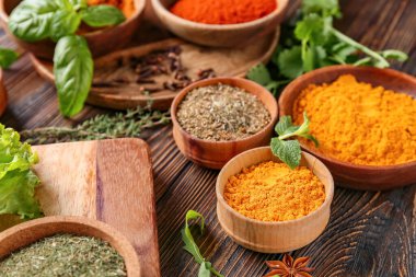 Ahşap arka planda farklı baharat ve otlarla dolu kaseler, yakın plan.