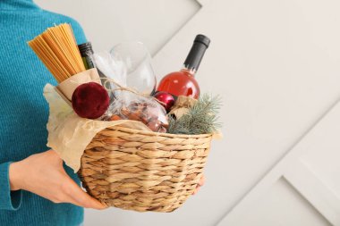 Elinde hediye sepeti olan gri arka planda ürünleri olan bir kadın.