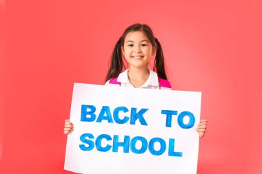 Renkli arka planda okula geri dönen küçük kız pankart tutuyor.