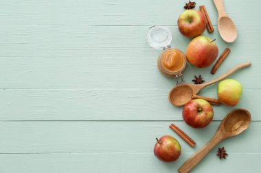Tatlı elma reçelli kavanoz, renkli ahşap arka planda kaşıklar ve baharatlar.