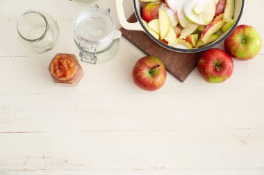 Reçelli kavanoz, kesilmiş elmalı tencere ve hafif arkaplanda şeker.