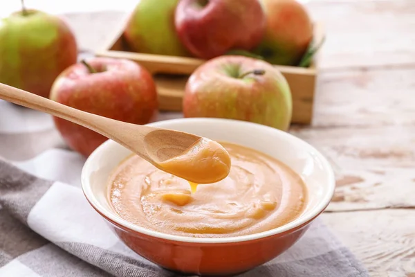 Bowl and spoon with sweet apple jam on wooden background