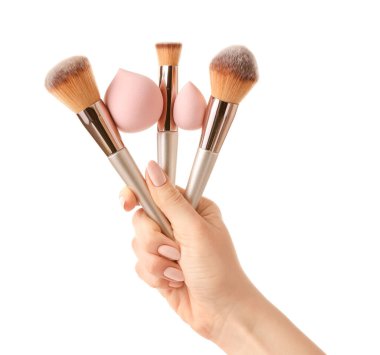 Beyaz arkaplanda makyaj süngerleri ve fırçalar olan el.