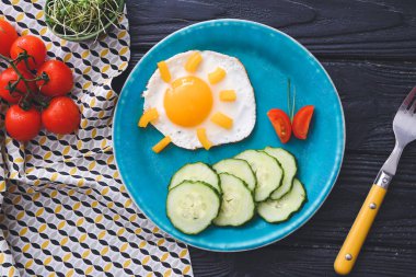 Koyu ahşap arka planda yumurta ve taze sebzeli çocuklar için yaratıcı bir kahvaltı.