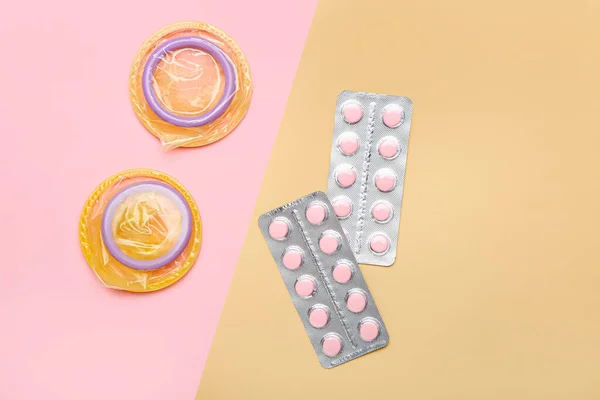 Open condoms and birth control pills on color background