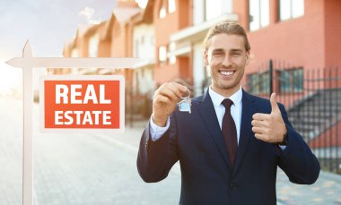 Anahtarı olan erkek emlakçı açık havada baş parmak hareketi yapıyor.