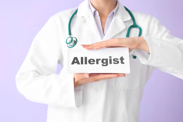 Doctor holding paper with word ALLERGIST on color background