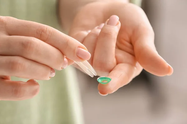 Female hands with tweezers and contact lens, closeup