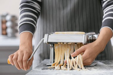 Mutfaktaki masada makineyle makarna yapan kadın.