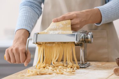 Mutfaktaki masada makineyle makarna yapan kadın.