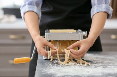 Mutfaktaki masada makineyle makarna yapan kadın.