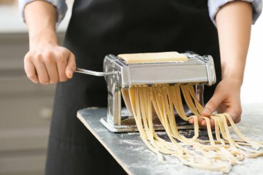 Mutfaktaki masada makineyle makarna yapan kadın.
