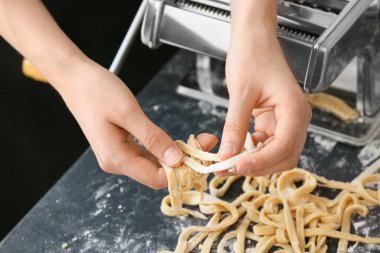 Mutfaktaki masada makineyle makarna yapan kadın.