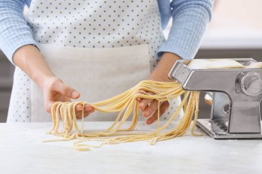 Mutfaktaki masada makineyle makarna yapan kadın.