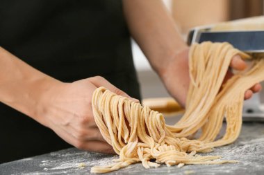 Mutfaktaki masada makineyle makarna yapan kadın.