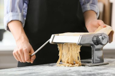 Mutfaktaki masada makineyle makarna yapan kadın.