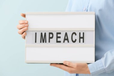 Renk arkaplanı üzerinde IMPEACH mesajı olan bir pano tutan kadın