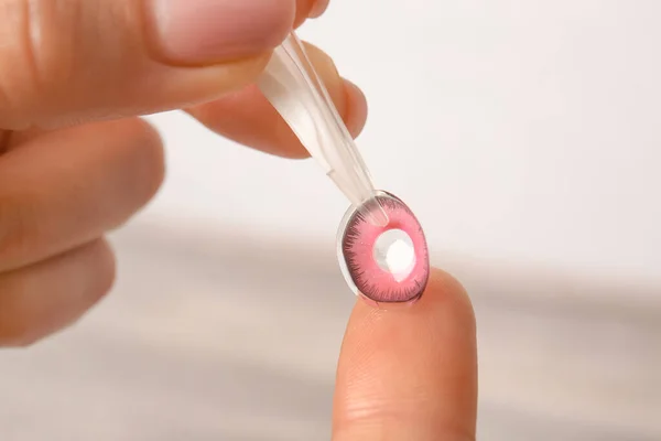 Female hands with tweezers and contact lens on light background