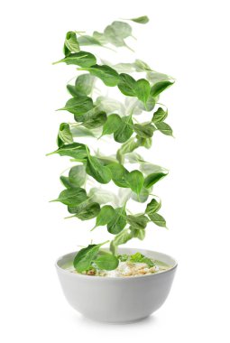 Lezzetli çorba ve beyaz arka planda düşen ıspanak yapraklarıyla dolu bir kase.