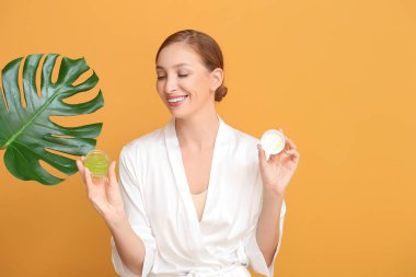 Kozmetik ürünleri ve renk arka planında tropikal yaprağı olan güzel genç bir kadın.