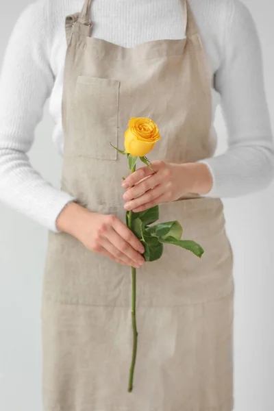 Female florist with beautiful yellow rose on light background