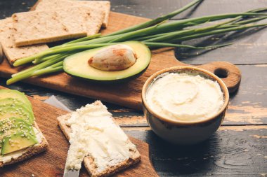 Lezzetli krem peynirli çıtır ekmek ve ahşap arka planda avokado.