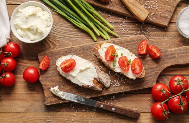 Lezzetli krem peynirli ekmek ve ahşap arka planda domates.