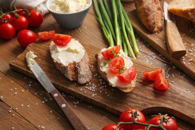 Lezzetli krem peynirli ekmek ve ahşap arka planda domates.