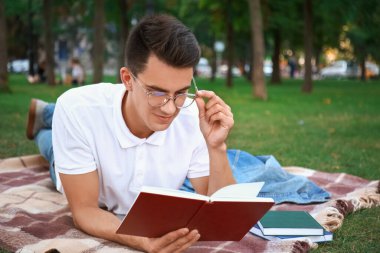 Genç adam parkta kitap okuyor.