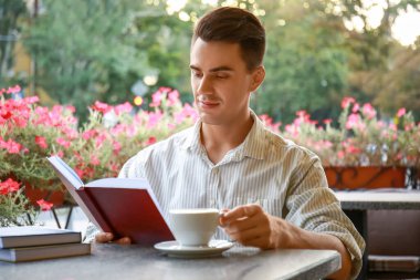 Kitaplı genç adam açık kafede kahve içiyor.