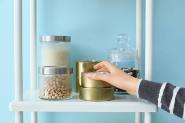 Mutfaktaki ürünlerle birlikte raflardan metal kutuları alan kadın.