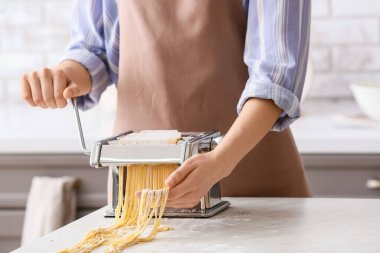 Mutfaktaki masada makineyle makarna yapan kadın.