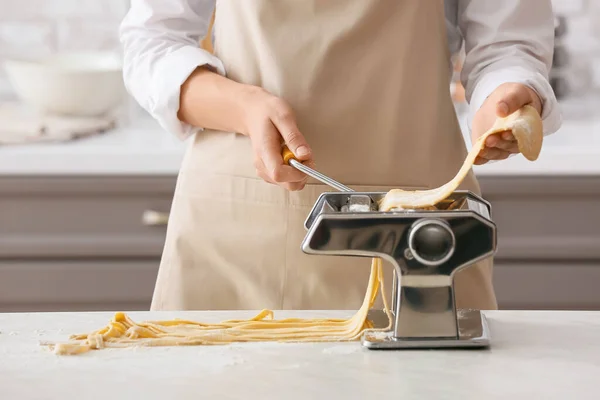 Woman making pasta with machine at table in kitchen