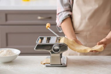 Mutfaktaki masada makineyle makarna yapan kadın.