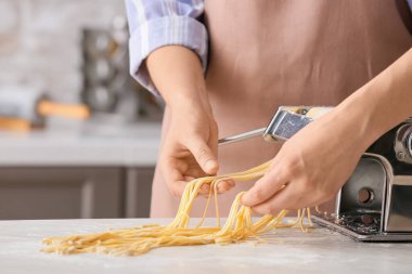 Mutfaktaki masada makineyle makarna yapan kadın.
