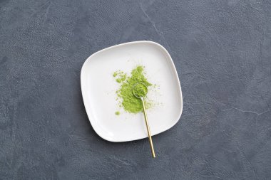 Koyu arkaplanda pudralanmış kibrit çayıyla tabak ve kepçe.