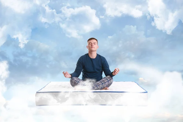 Young man meditating on mattress soft as clouds in blue sky