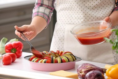 Mutfakta taze sebzeleri domates sosuyla giydiren bir kadın.