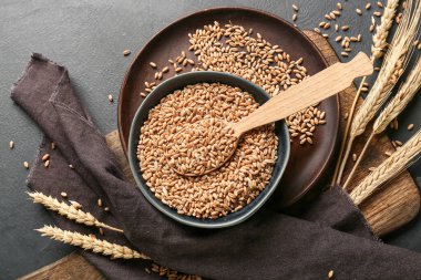 Koyu arkaplanda buğday taneleri olan kaşık ve kase.