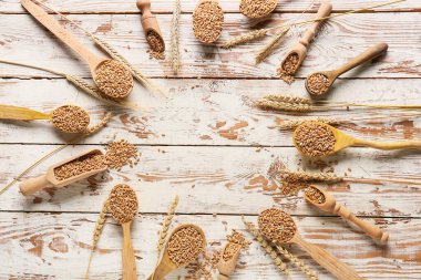 Kepçe ve kaşıktan yapılmış çerçeve, hafif ahşap arka planda buğday taneleri var.