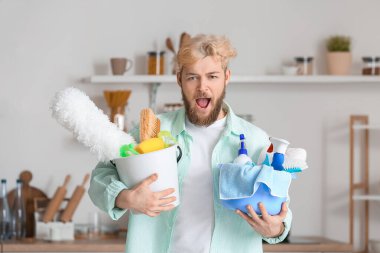 Mutfakta temizlik malzemesi olan kızgın genç bir adam.