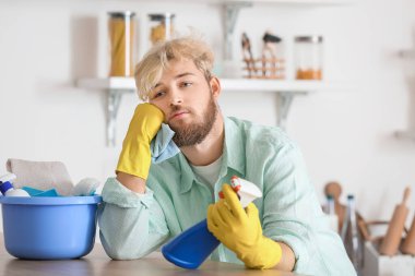Mutfakta temizlik malzemeleriyle yorgun genç bir adam.