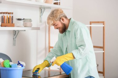 Genç adam mutfakta kızılötesi ocağı temizliyor.