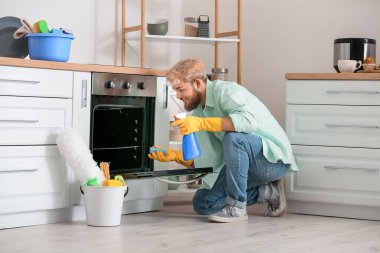 Genç adam mutfakta fırın temizliyor.