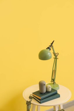 Odasında lamba ve renkli duvarın yanında kitaplar olan masa.