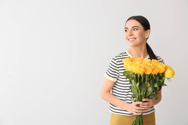 Gri arka planda gül buketi olan güzel genç bir kadın.