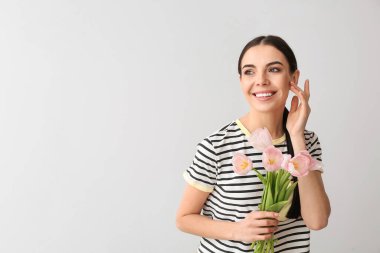 Gri arka planda çiçekleri olan güzel genç bir kadın.