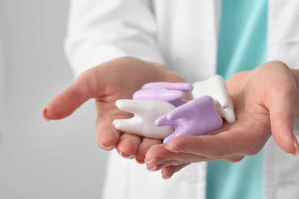 Female dentist with plastic teeth on light background, closeup